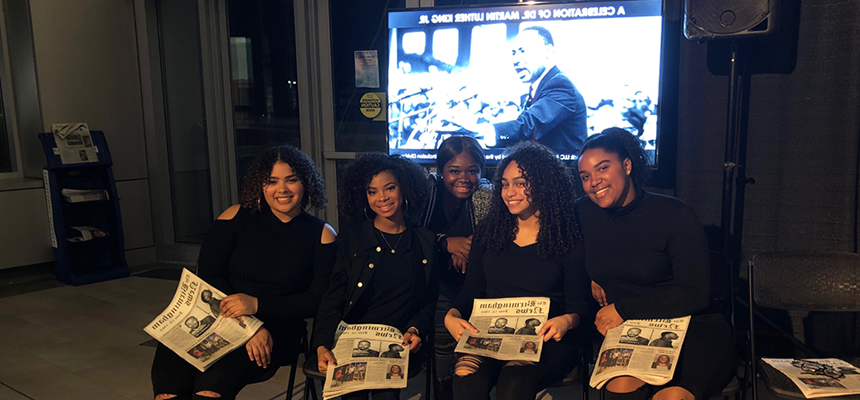 image of 5 students sitting in a row, holding a newspaper with a picture of Martin Luther King Jr. for a Black History Month performance.